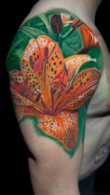 Detailed orange lily color tattoo on an upper arm