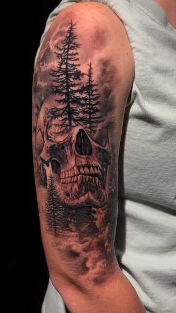 Photorealistic black-and-grey skull and pine forest tattoo on an upper arm