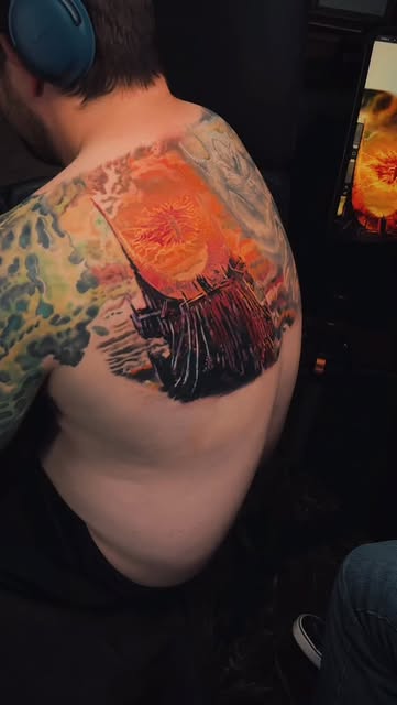 Color tattoo of a dark landscape beneath a glowing orange sky on a shoulder